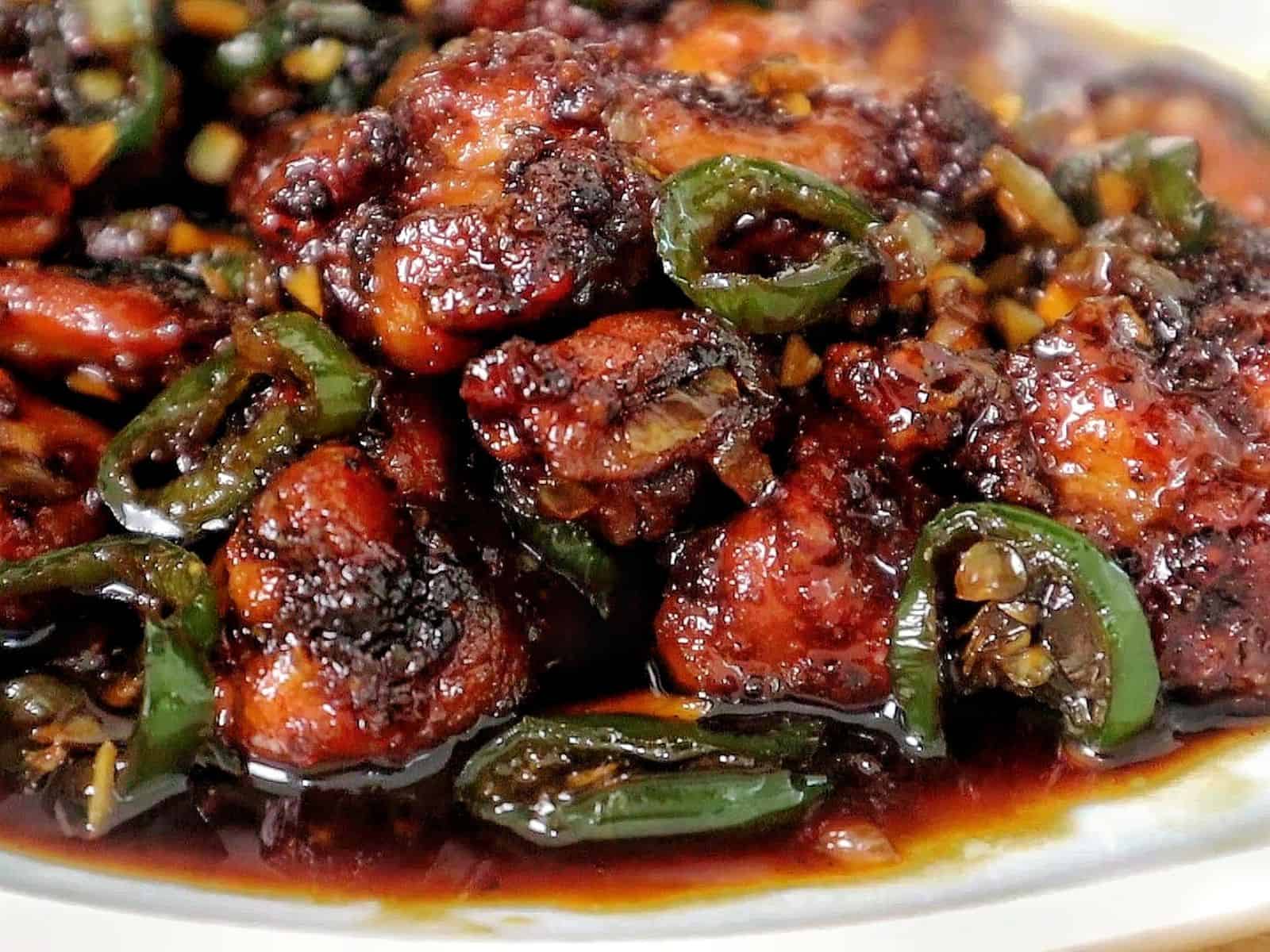 A plate of spicy jalapeño chicken thighs glazed in a honey, rich sauce, garnished with sliced jalapeños and minced garlic for a flavorful finish.