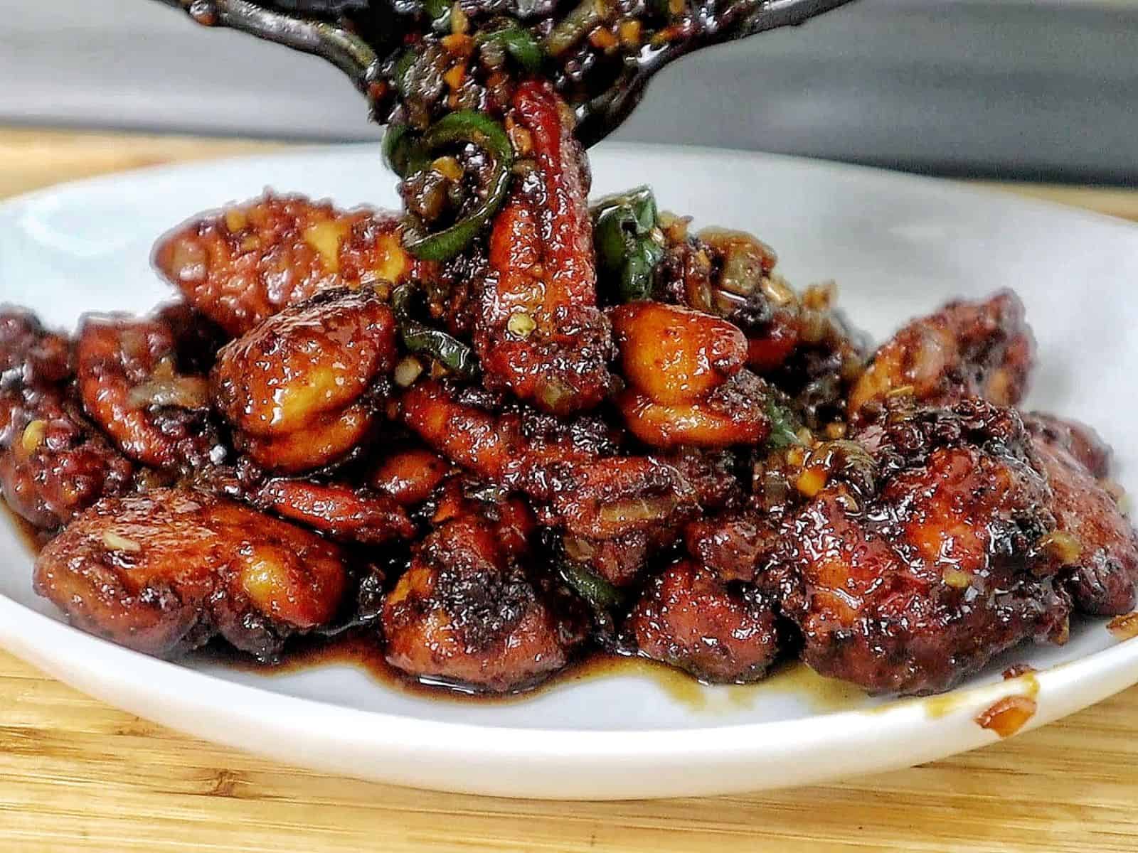 A plate of spicy jalapeño chicken thighs glazed in a honey, rich sauce, garnished with sliced jalapeños and minced garlic for a flavorful finish.