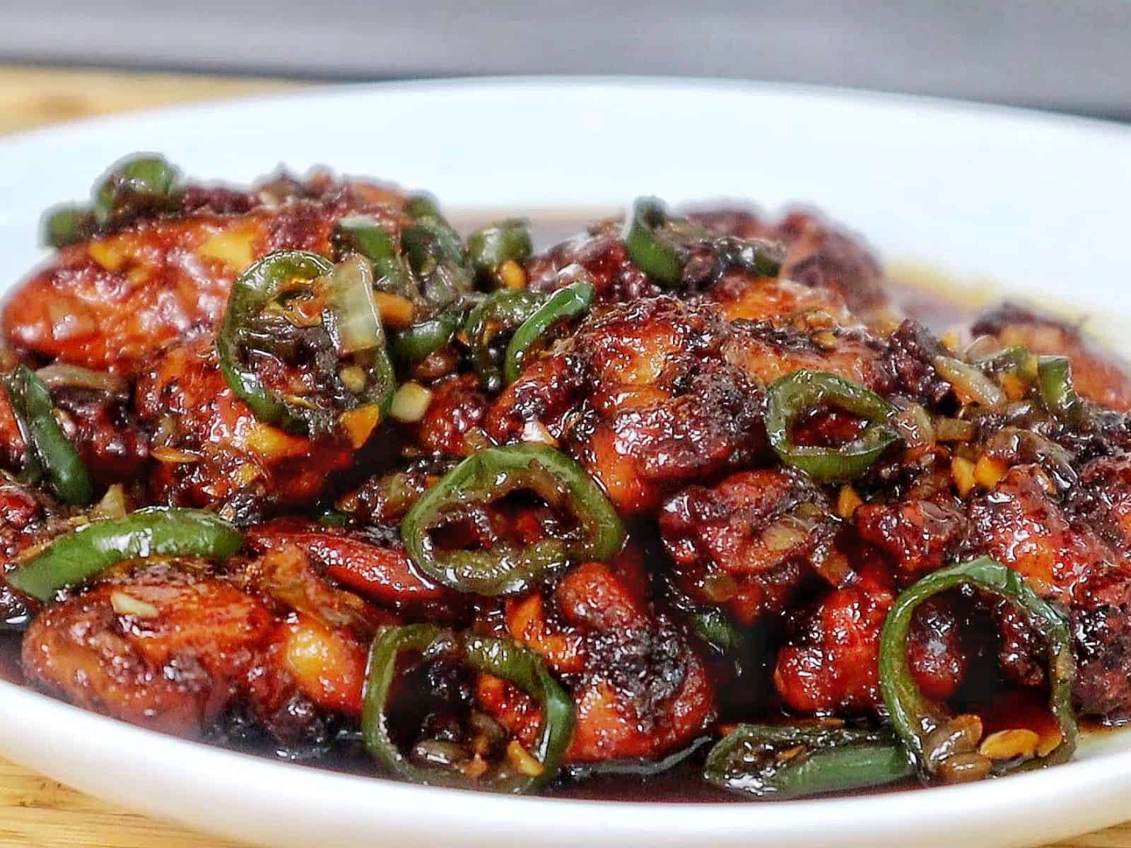 A plate of spicy jalapeño chicken thighs glazed in a honey, rich sauce, garnished with sliced jalapeños and minced garlic for a flavorful finish.