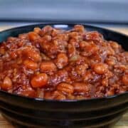 A cast-iron skillet filled with sweet and smoky baked beans simmering on a grill.
