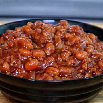 A cast-iron skillet filled with sweet and smoky baked beans simmering on a grill.