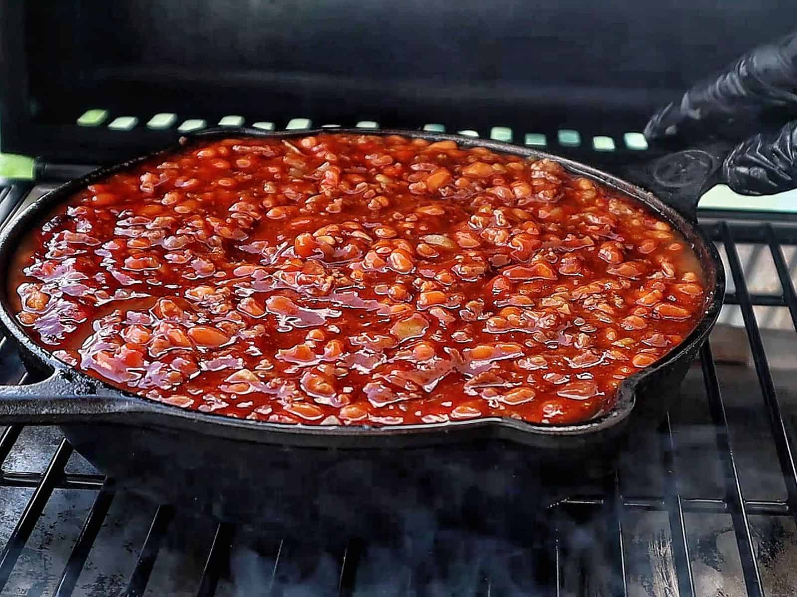 A cast-iron skillet filled with sweet and smoky baked beans simmering on a grill.