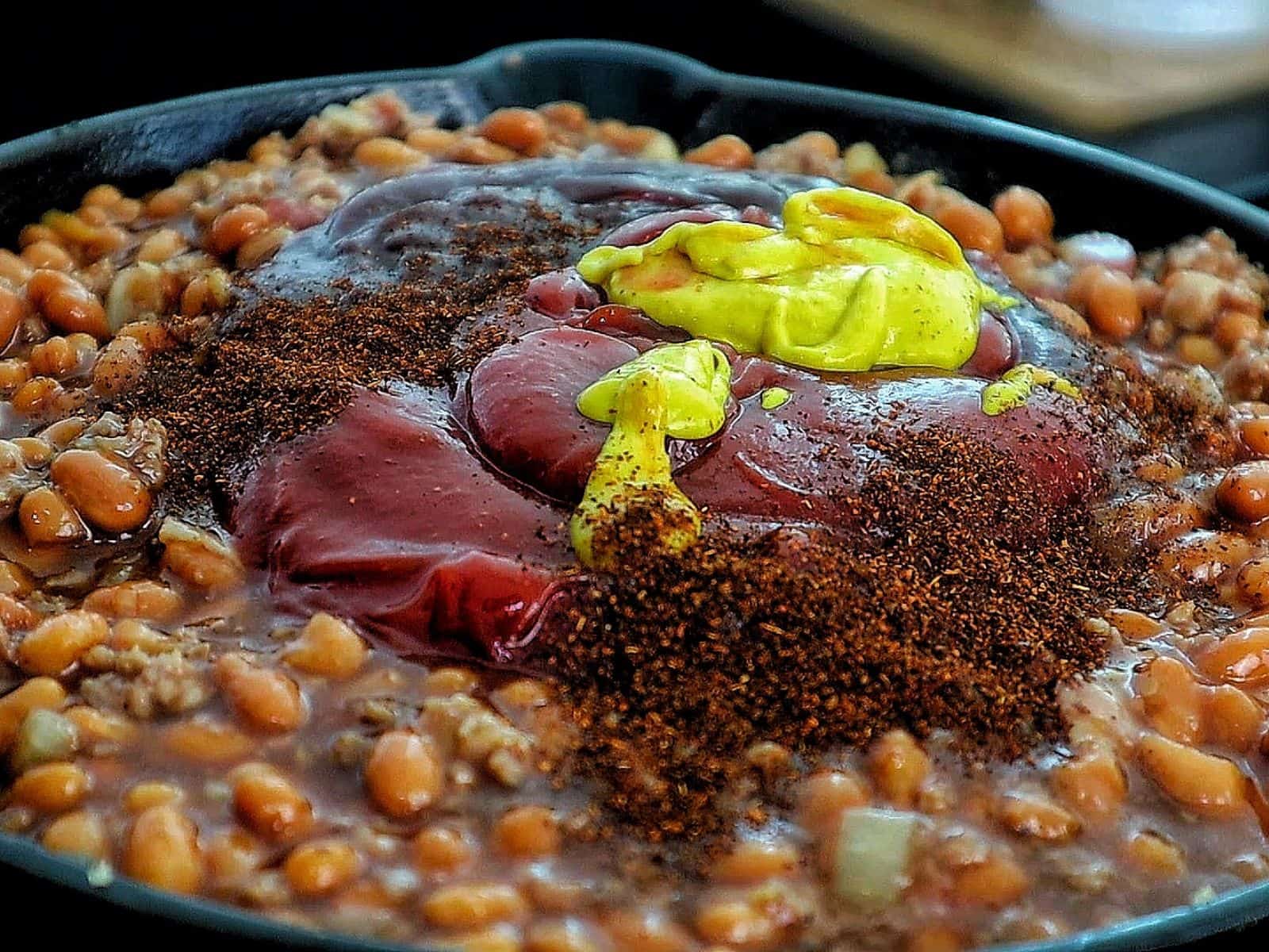 A cast-iron skillet filled with sweet and smoky baked beans simmering on a grill.
