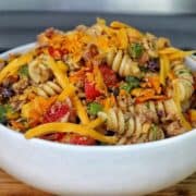 A bowl filled with taco pasta made with rotini noodles, ground beef, black beans, corn, tomatoes, green peppers, and topped with shredded cheddar cheese and crushed chips.