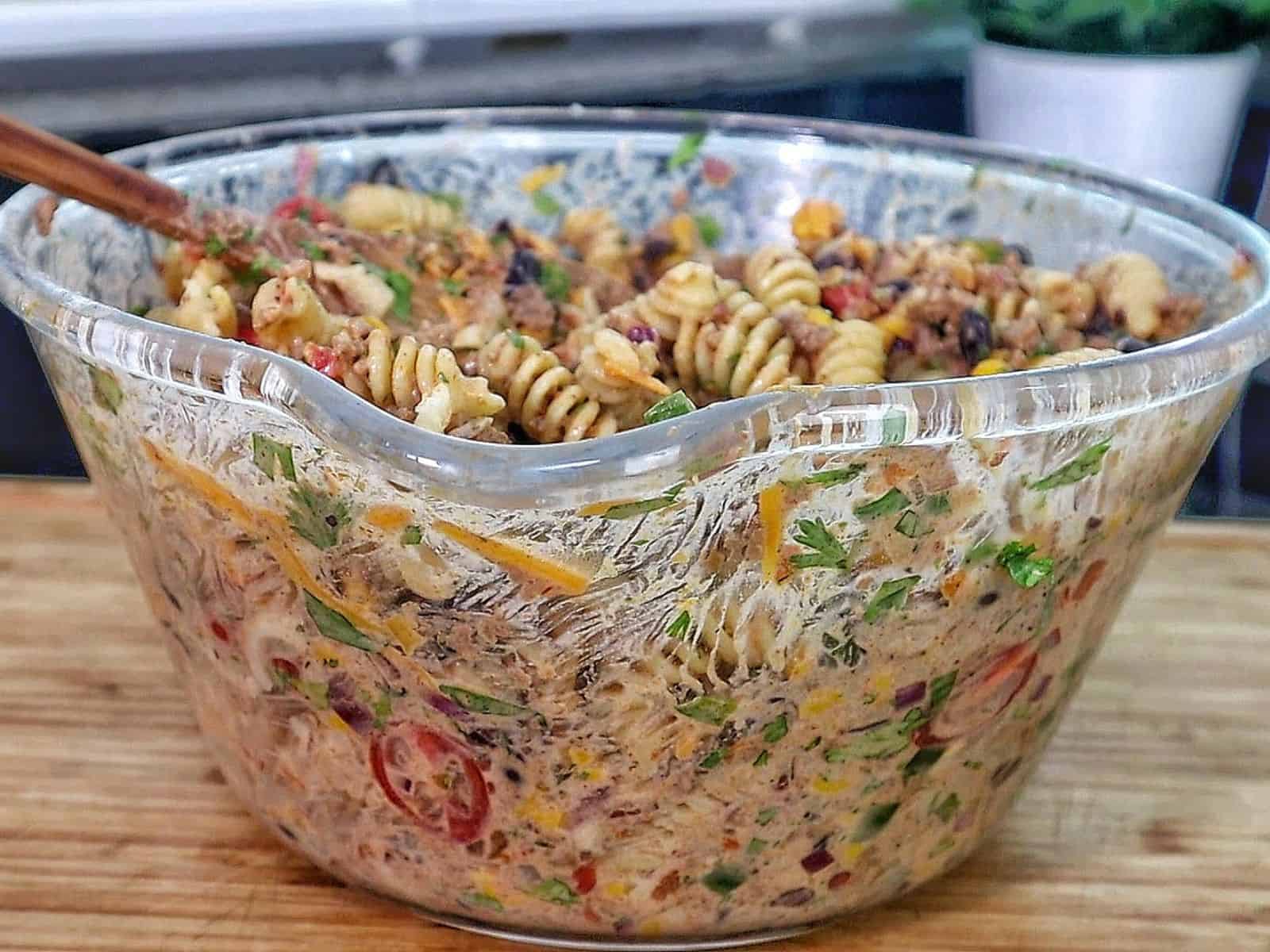 A bowl filled with taco pasta made with rotini noodles, ground beef, black beans, corn, tomatoes, green peppers, and topped with shredded cheddar cheese and crushed chips.