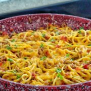 A skillet filled with cheesy taco spaghetti, featuring seasoned ground beef, spaghetti noodles, melted cheddar cheese, diced tomatoes, and garnished with chopped fresh parsley.