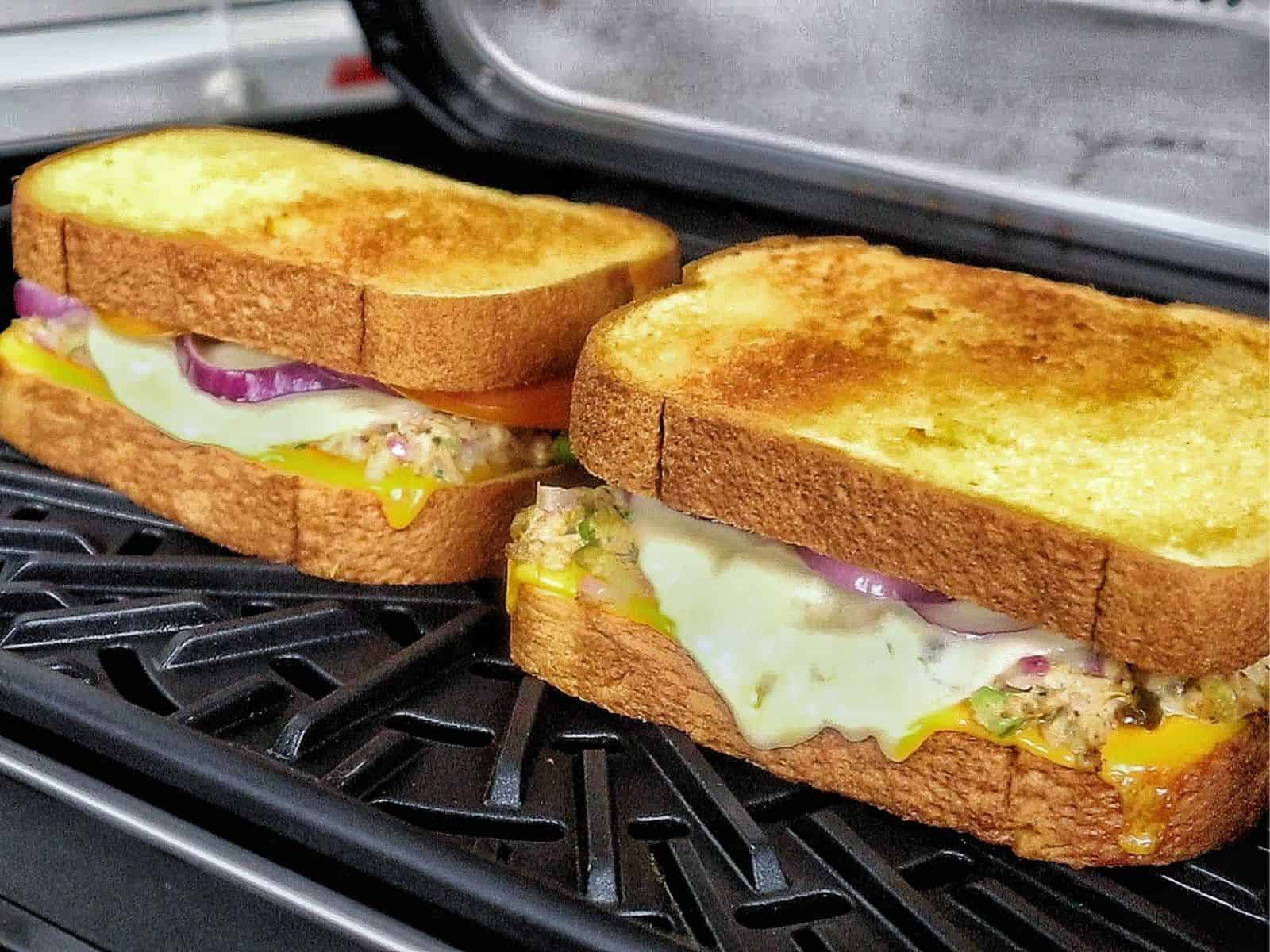 A golden-brown grilled tuna melt sandwich stacked in halves, oozing with melted cheddar cheese and filled with a creamy tuna salad mixture of tuna, onions, and celery.