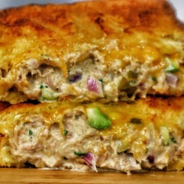 A golden-brown grilled tuna melt sandwich stacked in halves, oozing with melted cheddar cheese and filled with a creamy tuna salad mixture of tuna, onions, and celery.
