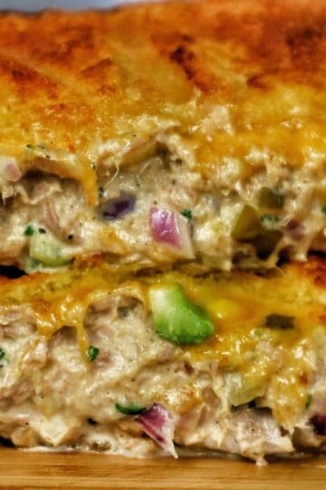 A golden-brown grilled tuna melt sandwich stacked in halves, oozing with melted cheddar cheese and filled with a creamy tuna salad mixture of tuna, onions, and celery.
