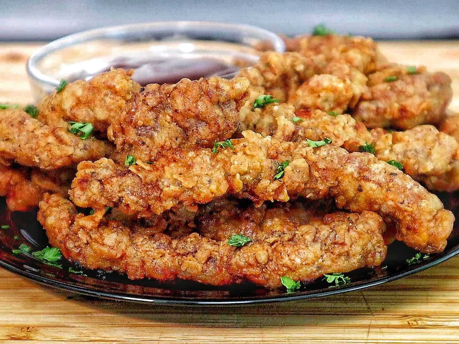 golden-brown crispy steak fingers, garnished with fresh parsley, served with a side of dipping sauce.