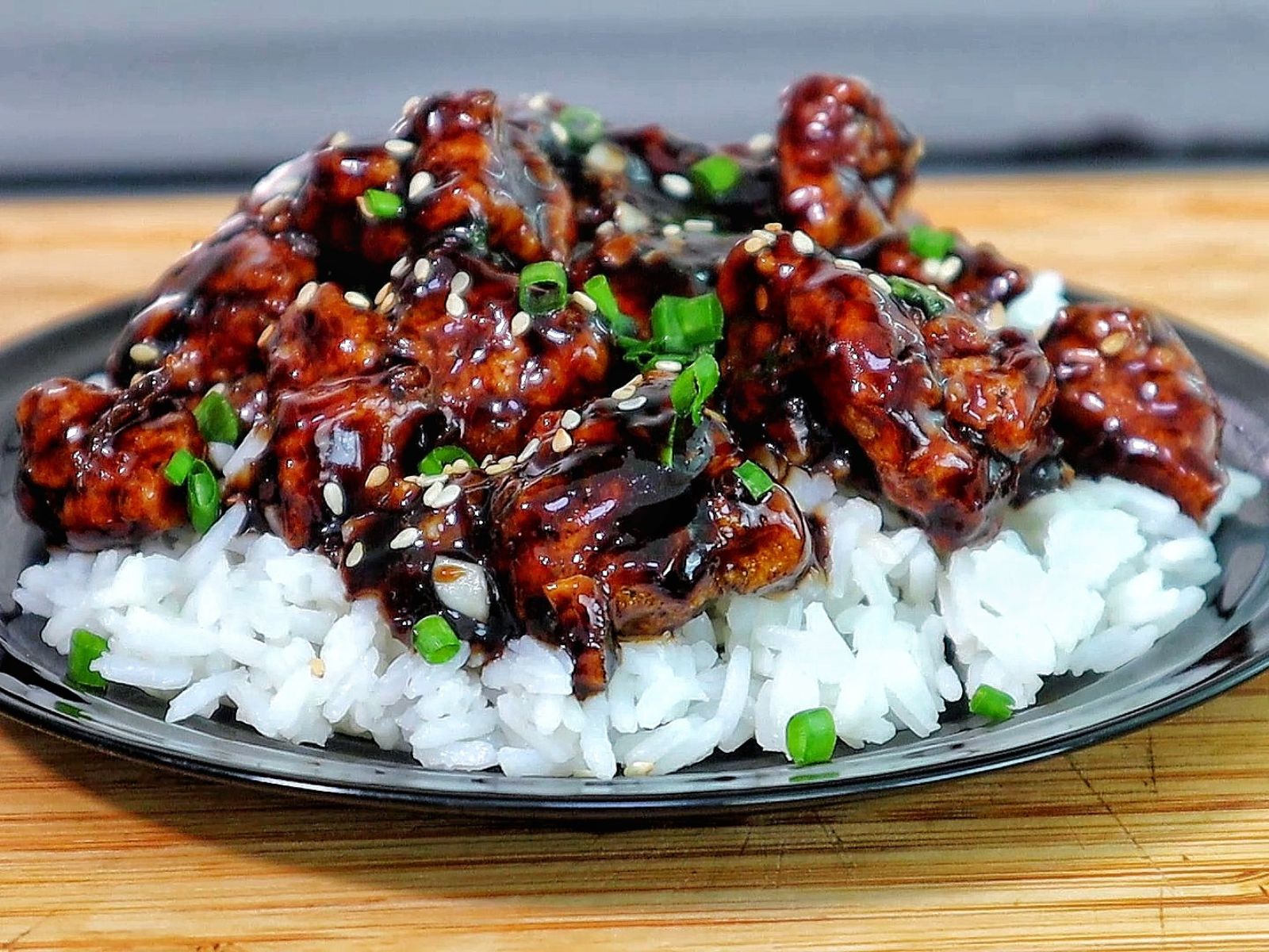Crispy Chinese orange chicken coated in a sticky orange glaze, garnished with sesame seeds and chopped green onions in a skillet.