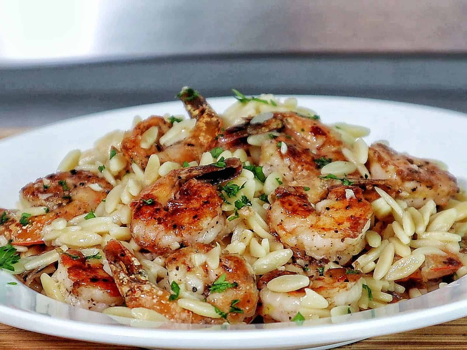A skillet filled with creamy orzo pasta and pan-seared shrimp, garnished with fresh parsley for a vibrant, comforting seafood pasta dish.