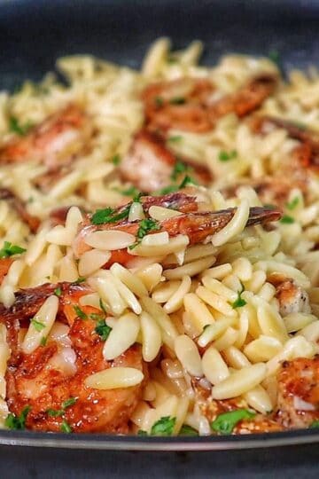 A skillet filled with creamy orzo pasta and pan-seared shrimp, garnished with fresh parsley for a vibrant, comforting seafood pasta dish.