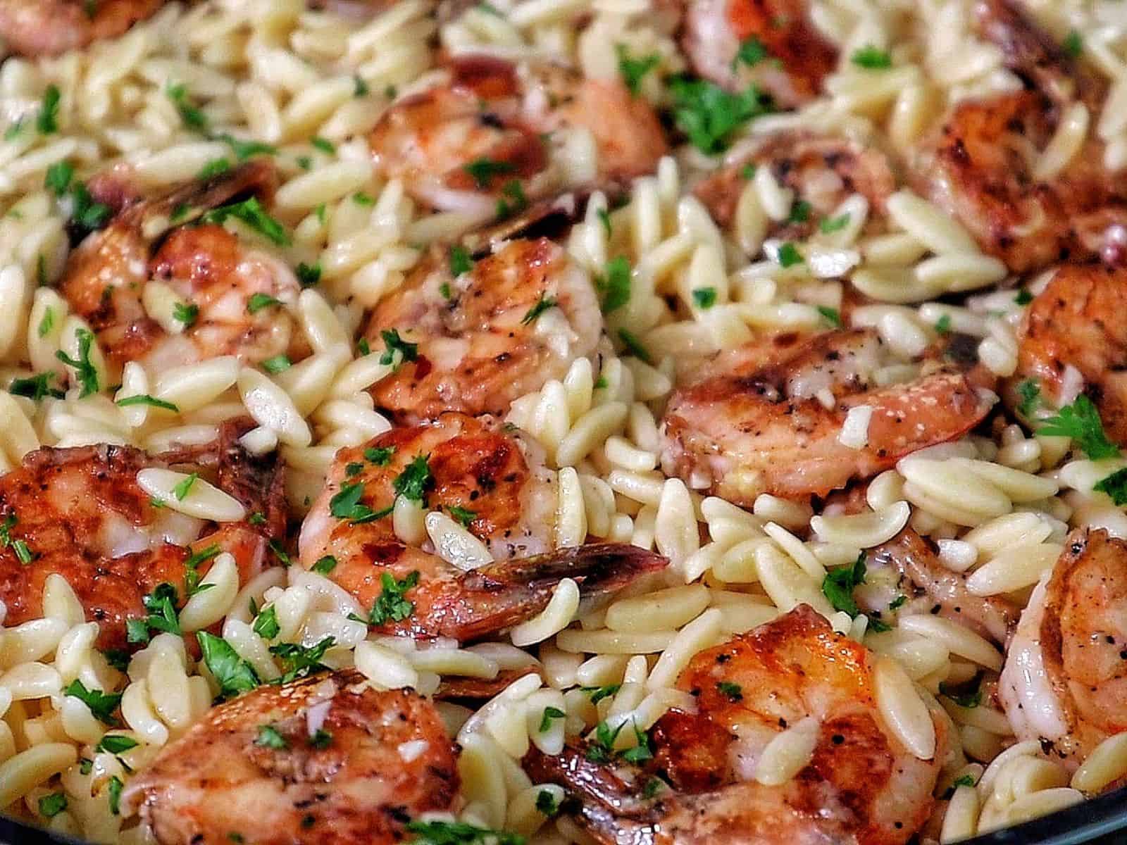 A skillet filled with creamy orzo pasta and pan-seared shrimp, garnished with fresh parsley for a vibrant, comforting seafood pasta dish.