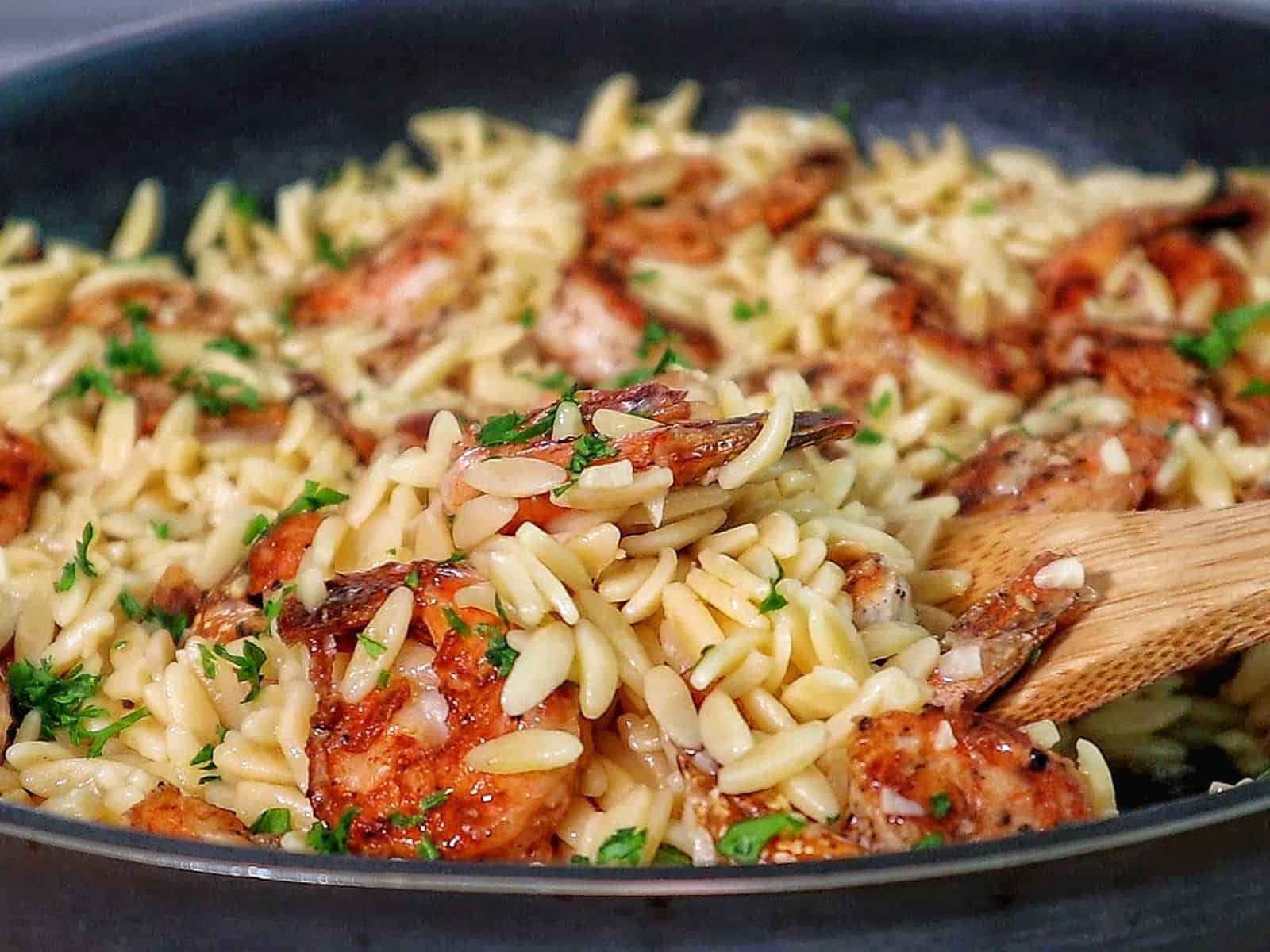 A skillet filled with creamy orzo pasta and pan-seared shrimp, garnished with fresh parsley for a vibrant, comforting seafood pasta dish.