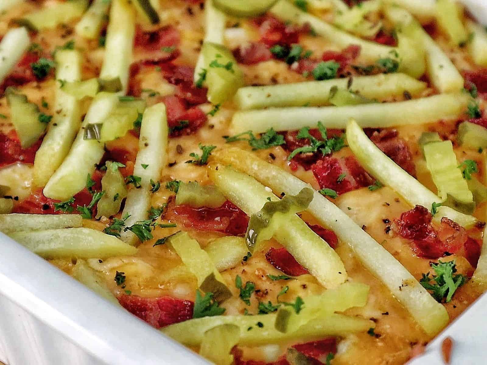 A golden-baked bacon cheeseburger casserole topped with melted cheese, crispy bacon pieces, pickle slices, and fresh parsley
