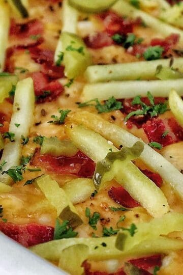 A golden-baked bacon cheeseburger casserole topped with melted cheese, crispy bacon pieces, pickle slices, and fresh parsley