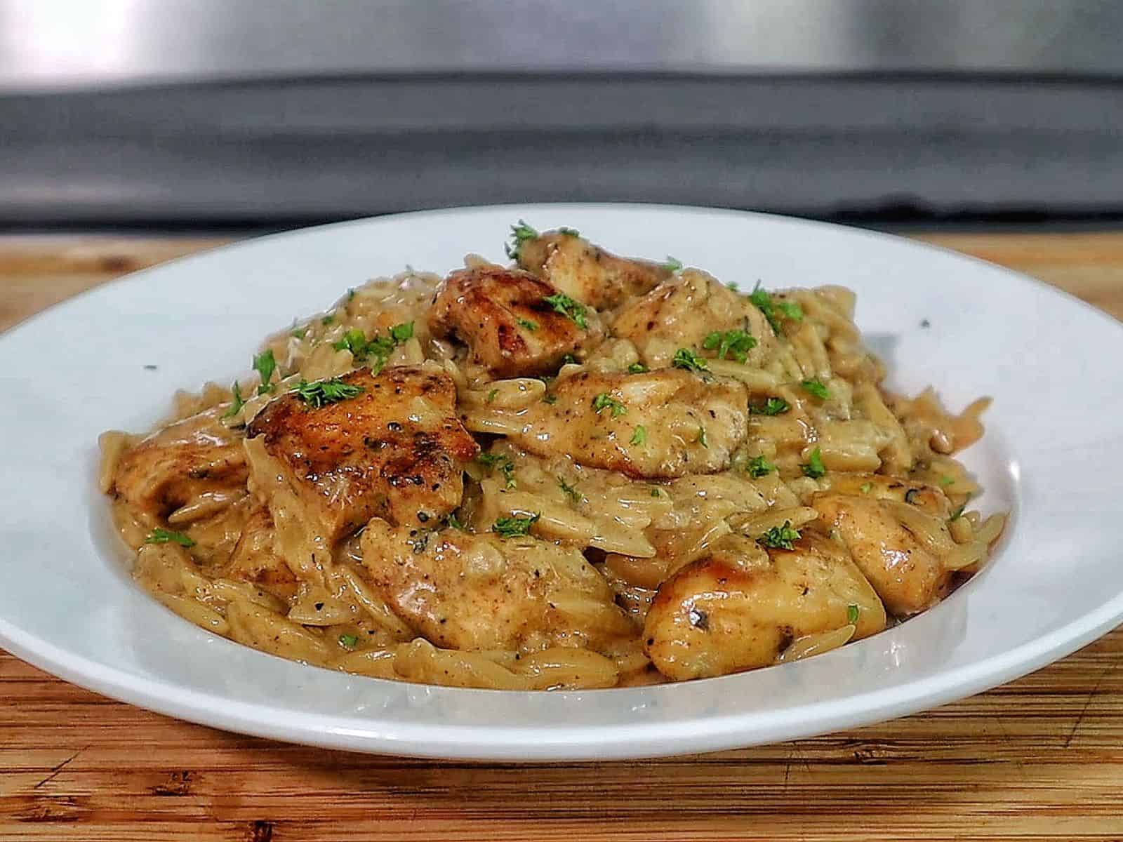 creamy cajun chicken alfredo orzo pasta, topped with golden seared chicken pieces and garnished with fresh herbs.