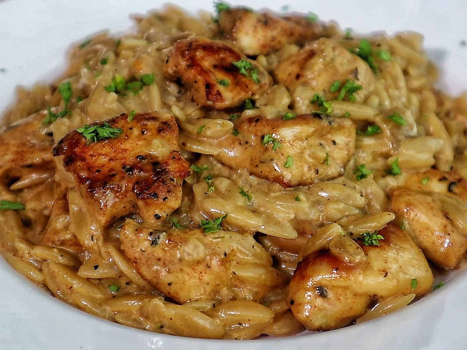 creamy cajun chicken alfredo orzo pasta, topped with golden seared chicken pieces and garnished with fresh herbs.
