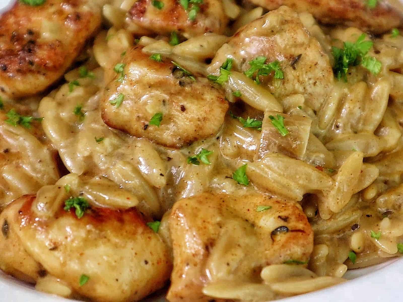 creamy cajun chicken alfredo orzo pasta, topped with golden seared chicken pieces and garnished with fresh herbs.