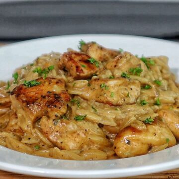 creamy cajun chicken alfredo orzo pasta, topped with golden seared chicken pieces and garnished with fresh herbs.