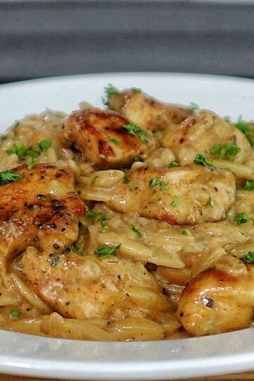 creamy cajun chicken alfredo orzo pasta, topped with golden seared chicken pieces and garnished with fresh herbs.