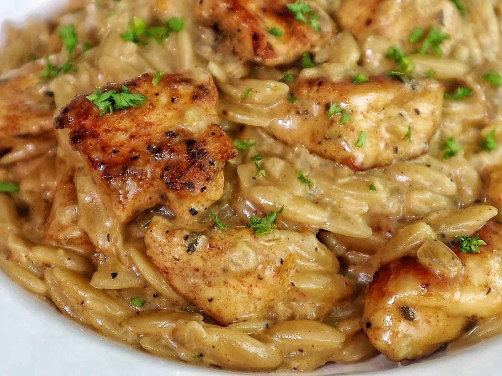 creamy cajun chicken alfredo orzo pasta, topped with golden seared chicken pieces and garnished with fresh herbs.