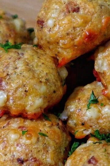 Cheesy Parmesan Mozzarella Bacon Bites stacked on a wooden board, garnished with fresh parsley, showcasing a cheesy, crispy texture.
