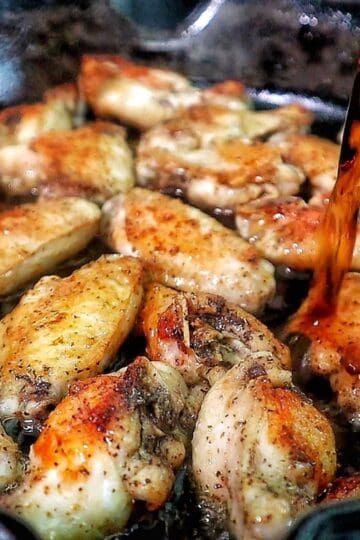 Glazed Coca-Cola chicken wings coated in a sticky, caramelized sauce, garnished with sliced green onions.