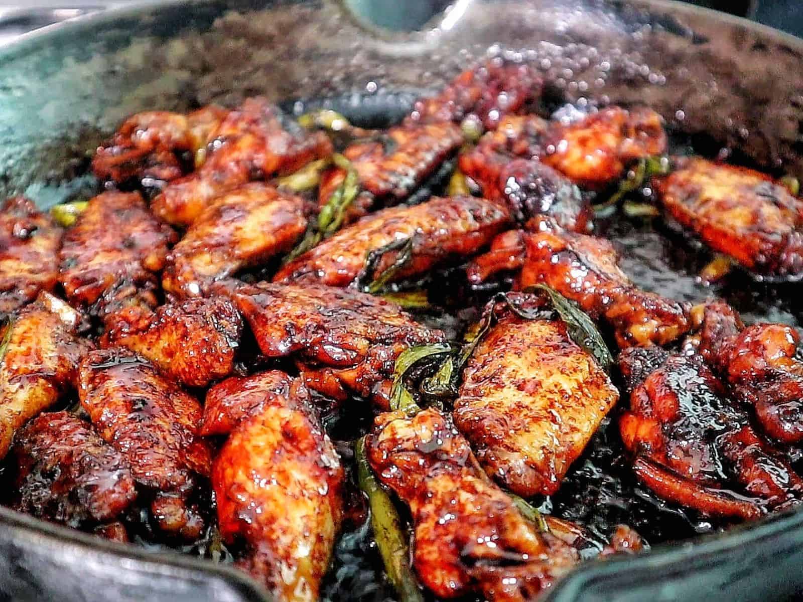 Glazed Coca-Cola chicken wings coated in a sticky, caramelized sauce, garnished with sliced green onions.