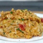 A creamy serving of one pot queso chicken and rice topped with melted cheese and fresh herbs, scooped from a skillet