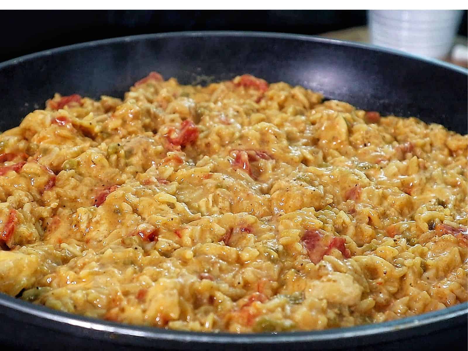 A creamy serving of one pot queso chicken and rice topped with melted cheese and fresh herbs, scooped from a skillet