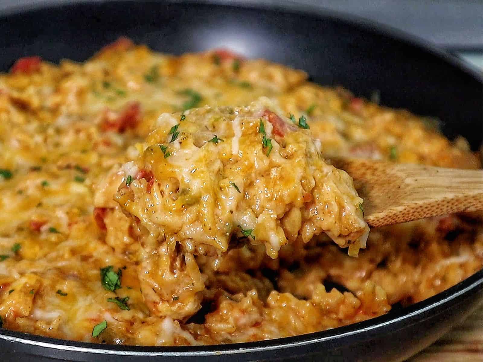 A creamy serving of one pot queso chicken and rice topped with melted cheese and fresh herbs, scooped from a skillet