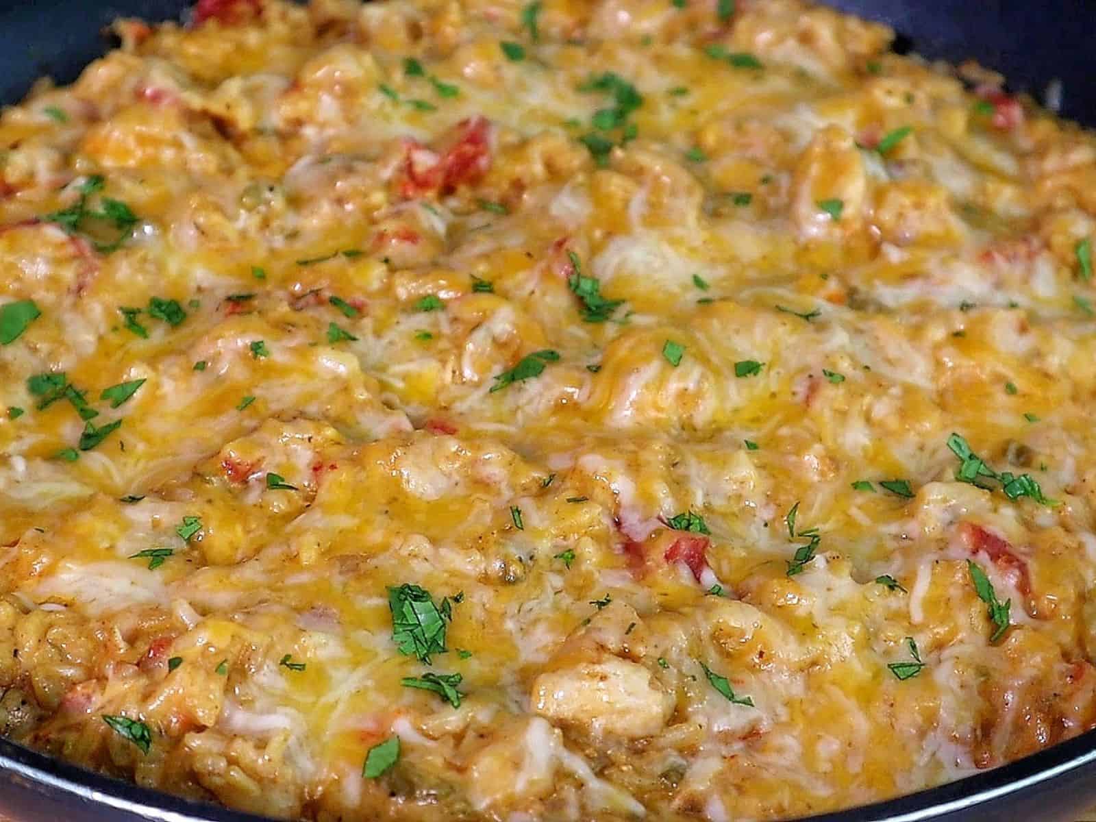 A creamy serving of one pot queso chicken and rice topped with melted cheese and fresh herbs, scooped from a skillet
