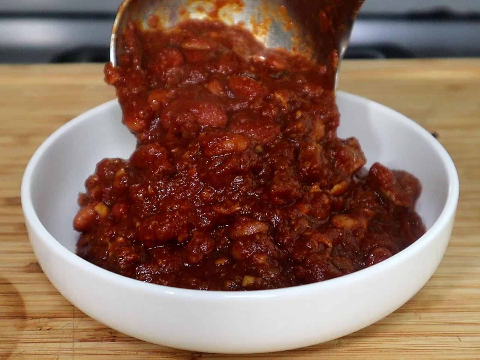 A hearty bowl of steak chili topped with shredded cheddar cheese, chopped red onions, jalapeño slices, and a dollop of sour cream, served hot and ready to eat.