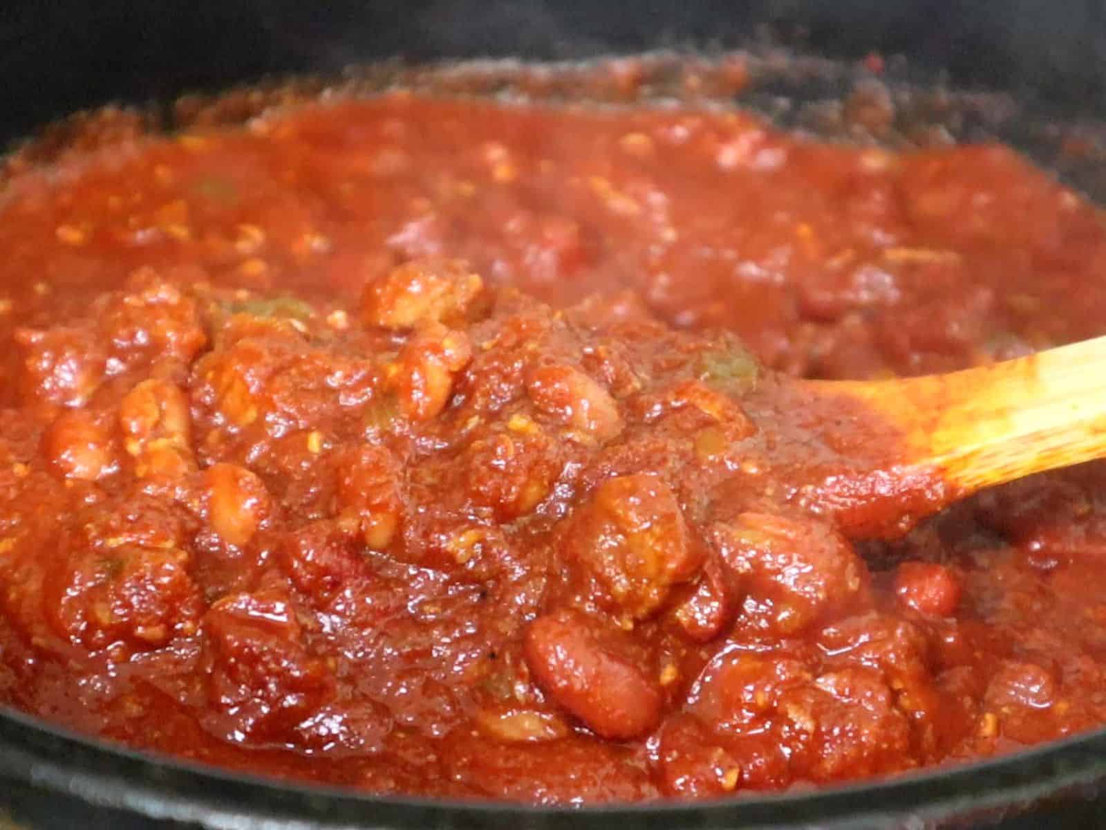 A hearty bowl of steak chili topped with shredded cheddar cheese, chopped red onions, jalapeño slices, and a dollop of sour cream, served hot and ready to eat.