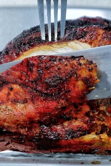 A golden brown air fryer turkey breast seasoned with a dark caramelized crust and juices pooling at the bottom.