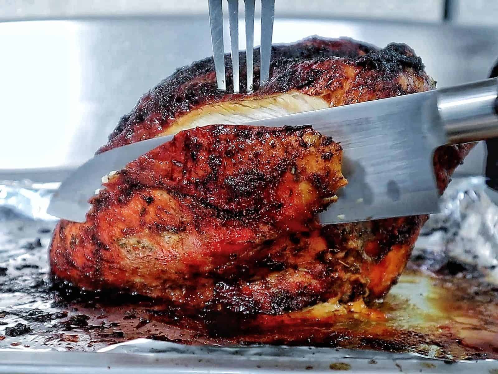 A golden brown air fryer turkey breast seasoned with a dark caramelized crust and juices pooling at the bottom.