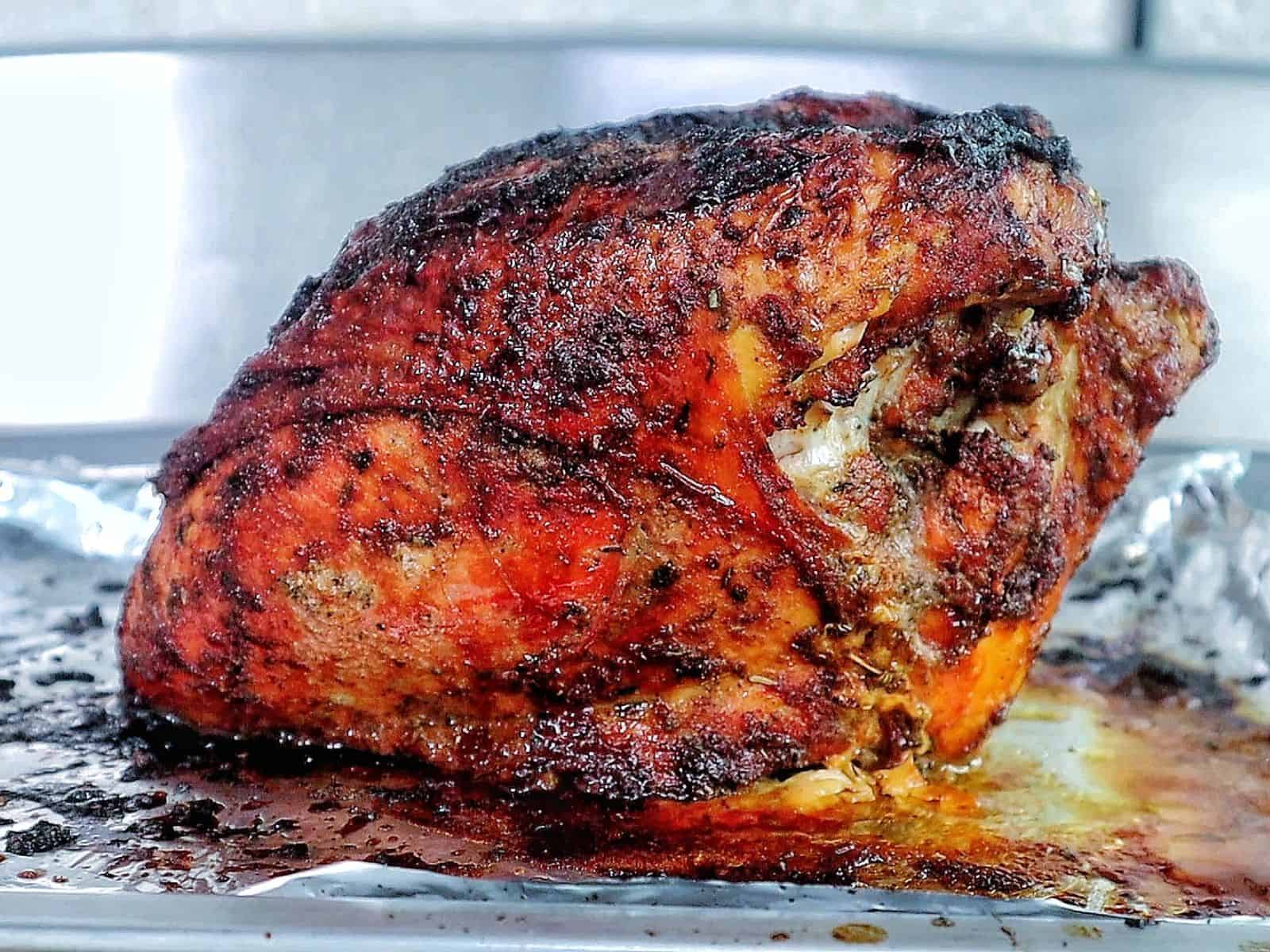 A golden brown air fryer turkey breast seasoned with a dark caramelized crust and juices pooling at the bottom.