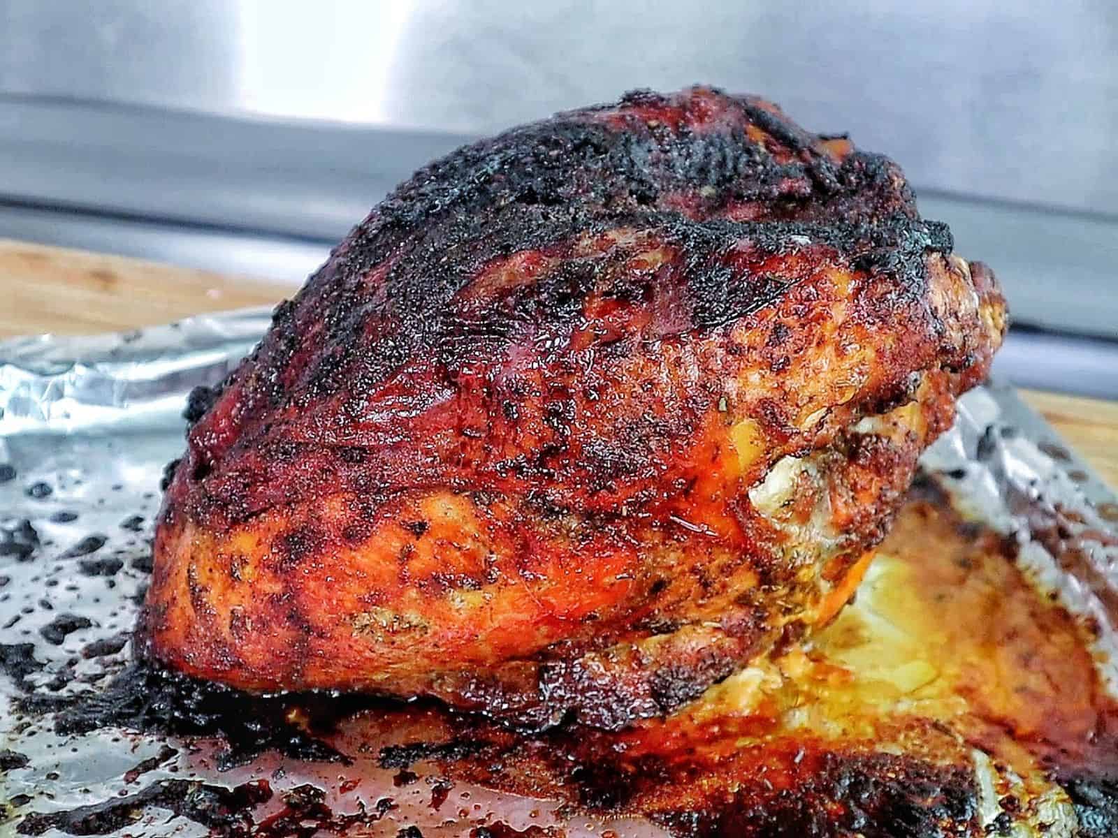 A golden brown air fryer turkey breast seasoned with a dark caramelized crust and juices pooling at the bottom.