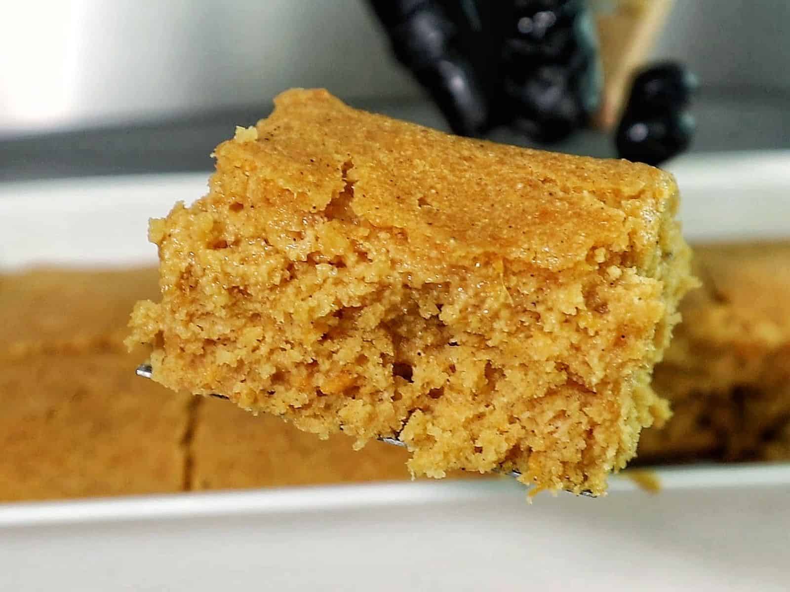 Two thick slices of brown sugar sweet potato cornbread stacked on a black plate, topped with melted butter and drizzled syrup. 