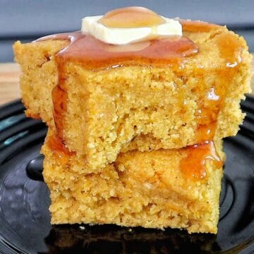 Two thick slices of brown sugar sweet potato cornbread stacked on a black plate, topped with melted butter and drizzled syrup.