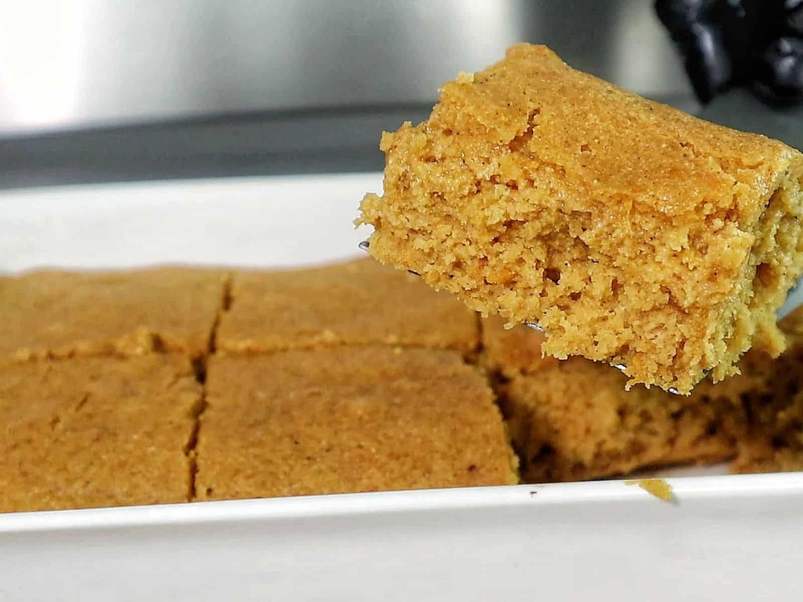 Two thick slices of brown sugar sweet potato cornbread stacked on a black plate, topped with melted butter and drizzled syrup. 