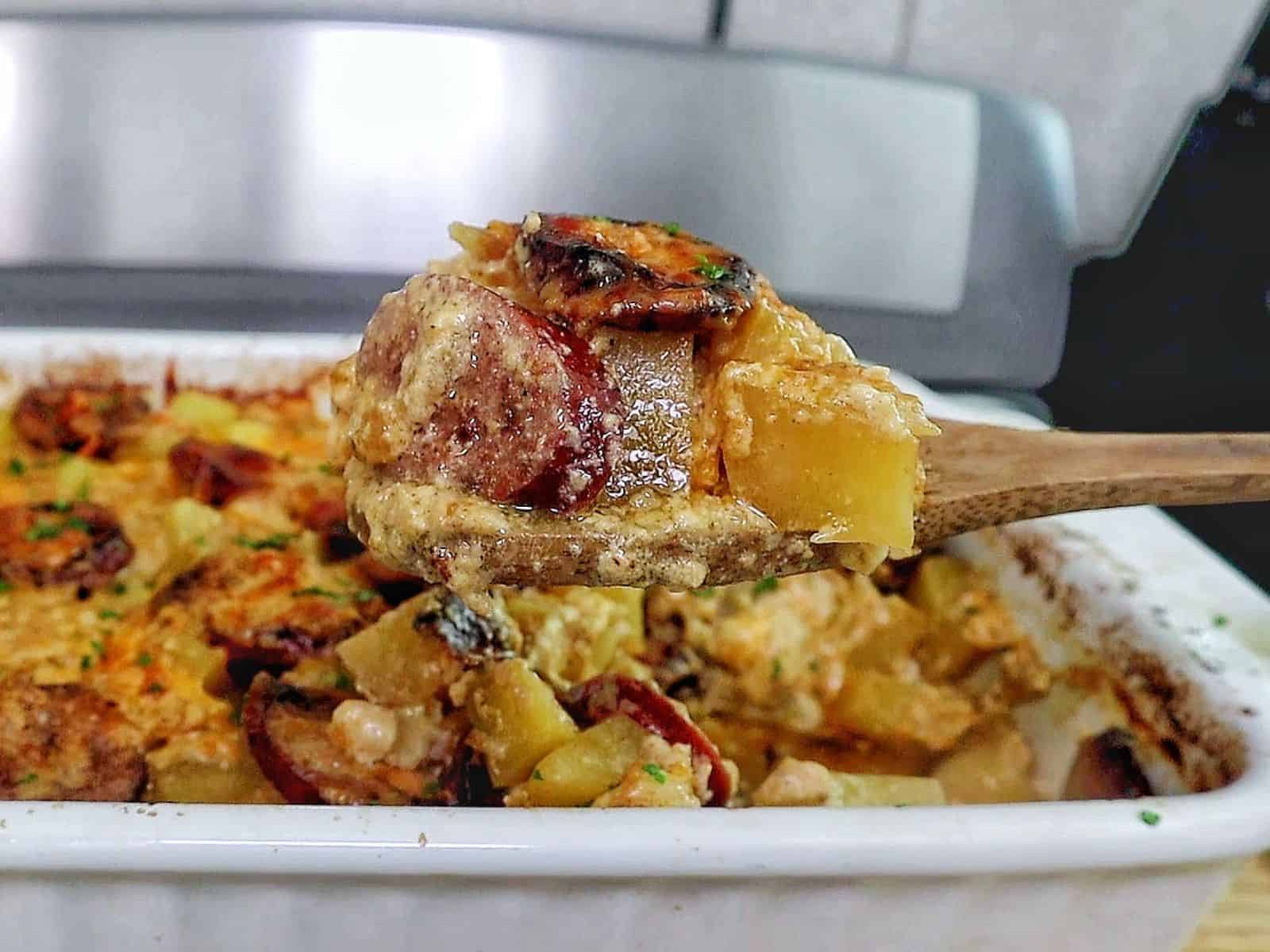 Cheesy sausage and potato casserole, featuring golden melted cheese, browned sausage slices, and tender potato cubes scooped from a baking dish.
