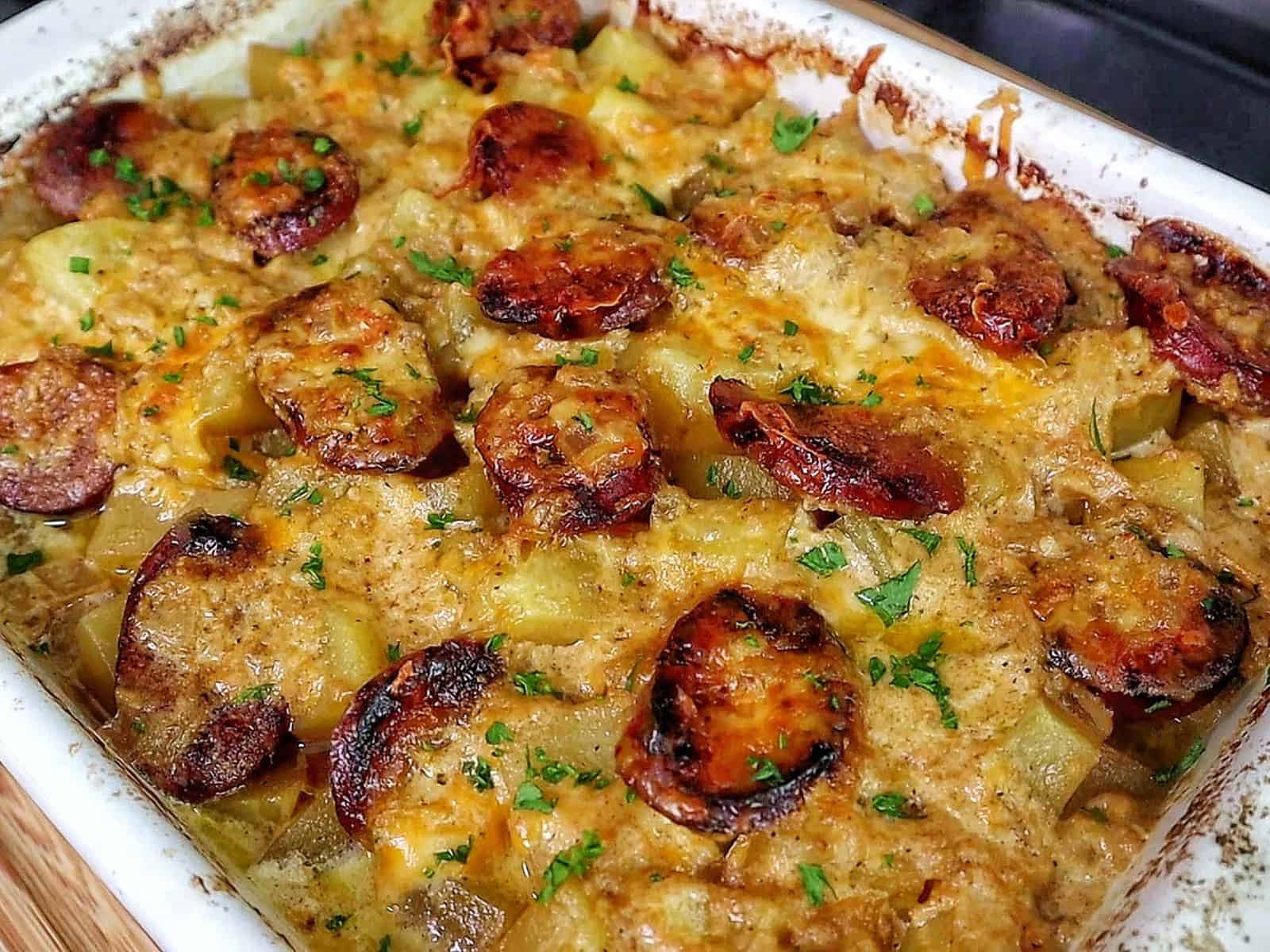 Cheesy sausage and potato casserole, featuring golden melted cheese, browned sausage slices, and tender potato cubes scooped from a baking dish.