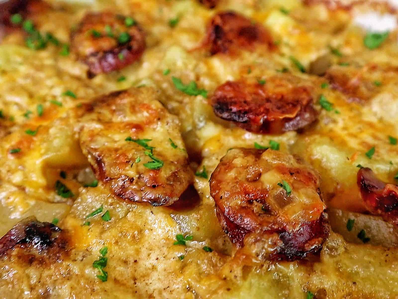 Cheesy sausage and potato casserole, featuring golden melted cheese, browned sausage slices, and tender potato cubes scooped from a baking dish.