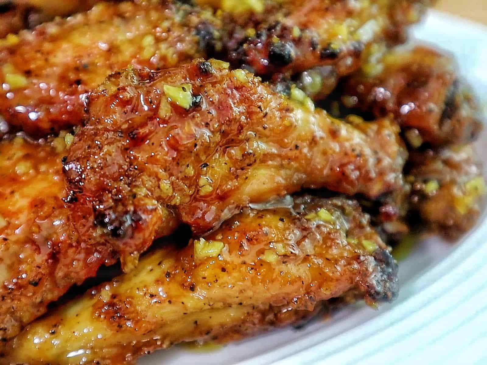 A plate filled with crispy honey lemon pepper chicken wings tossed in a lemon pepper sauce, served alongside jalapeño poppers stuffed with a cheesy bacon filling.