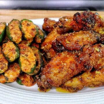 A plate filled with crispy honey lemon pepper chicken wings tossed in a lemon pepper sauce, served alongside jalapeño poppers stuffed with a cheesy bacon filling.