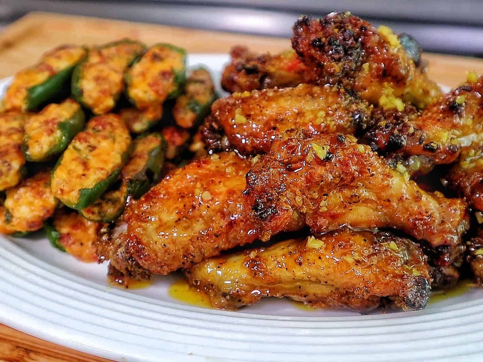 A plate filled with crispy honey lemon pepper chicken wings tossed in a lemon pepper sauce, served alongside jalapeño poppers stuffed with a cheesy bacon filling.