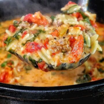 A creamy bowl of sausage orzo soup filled with tomatoes, spinach, and tender pasta, topped with fresh basil and melted Parmesan.